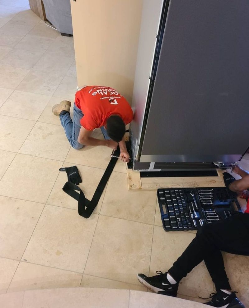 Two people installing a large, dark panel. One kneels, securing a strap; the other works on the base with tools.