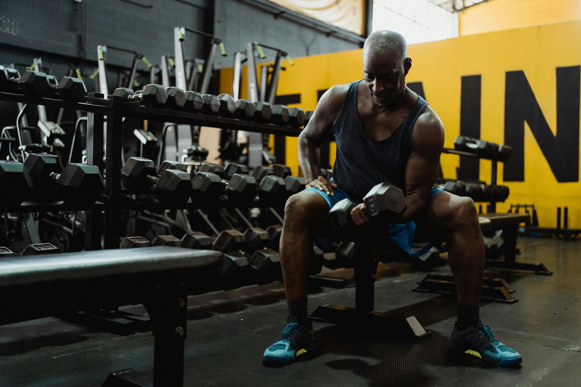 A man is sitting on a bench in a gym holding a dumbbell.