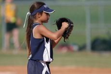 A young girl is holding a baseball glove on a field.