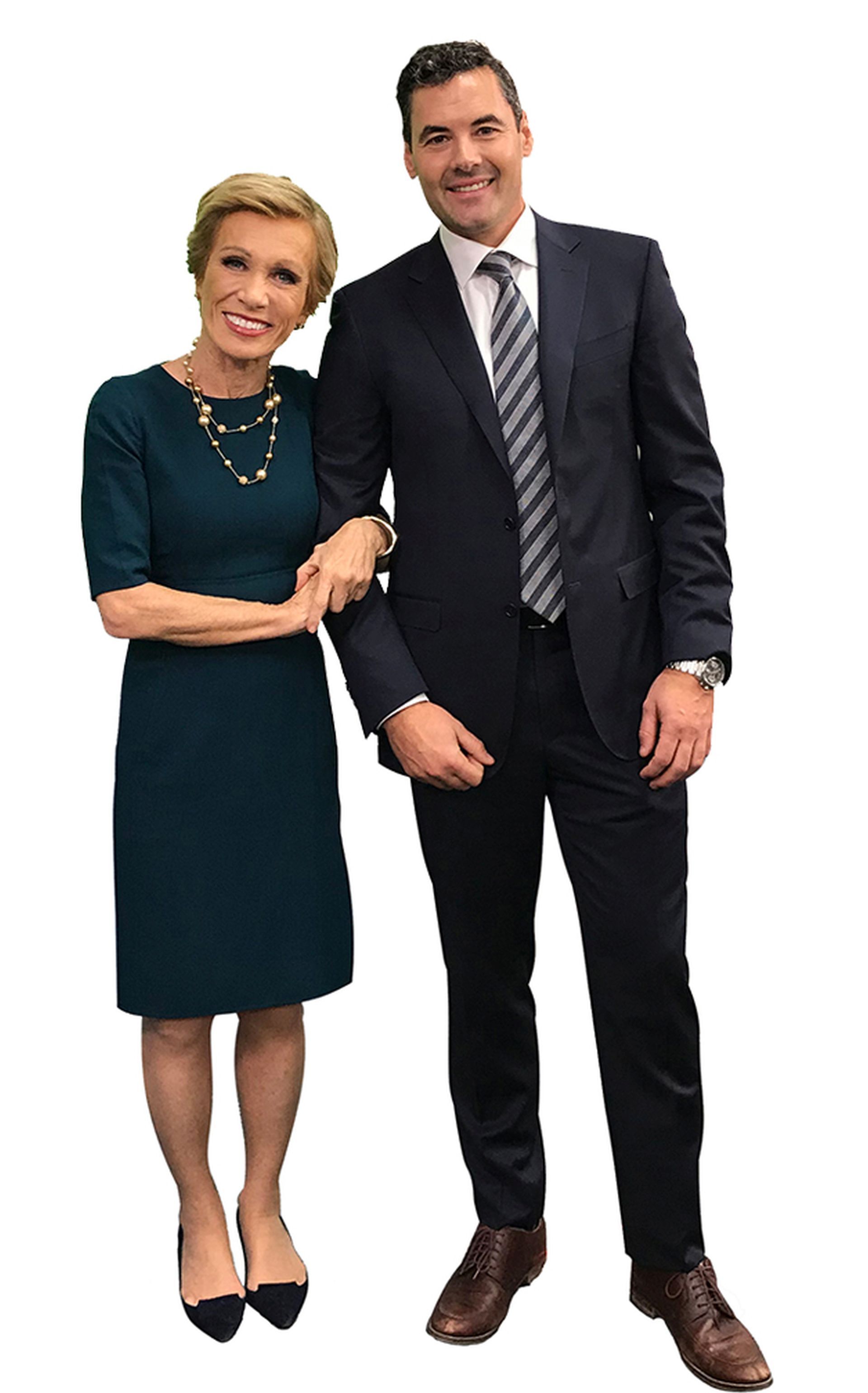 A smiling woman in a dark teal dress links arms with a man in a dark suit and striped tie against a white background.