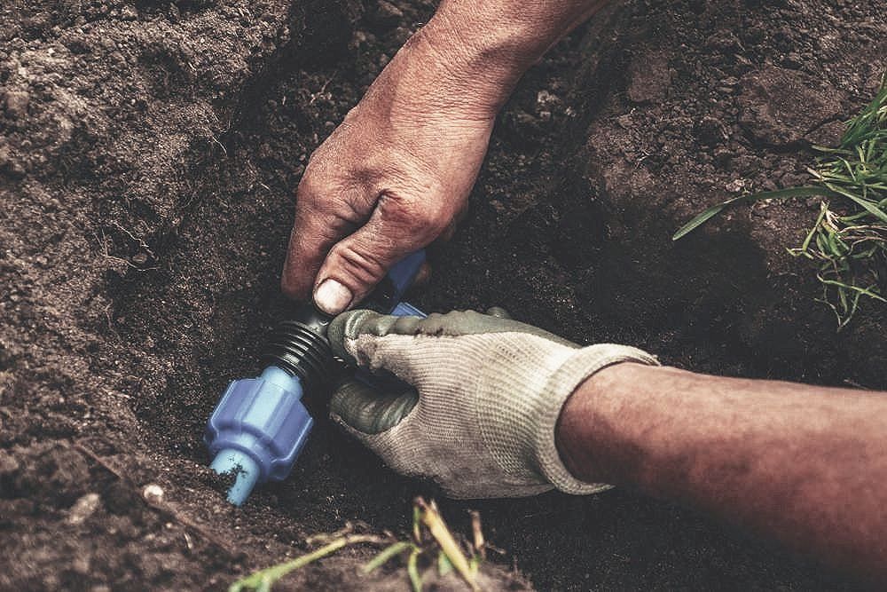 A Person Is Fixing a Hose in The Dirt — Top To Bottom Plumbing in Garbutt, QLD