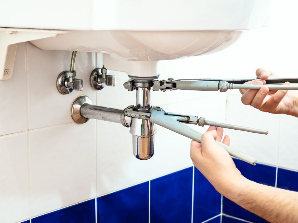 A Man Is Fixing a Faucet in A Bathroom with A Wrench — Top To Bottom Plumbing in Garbutt, QLD