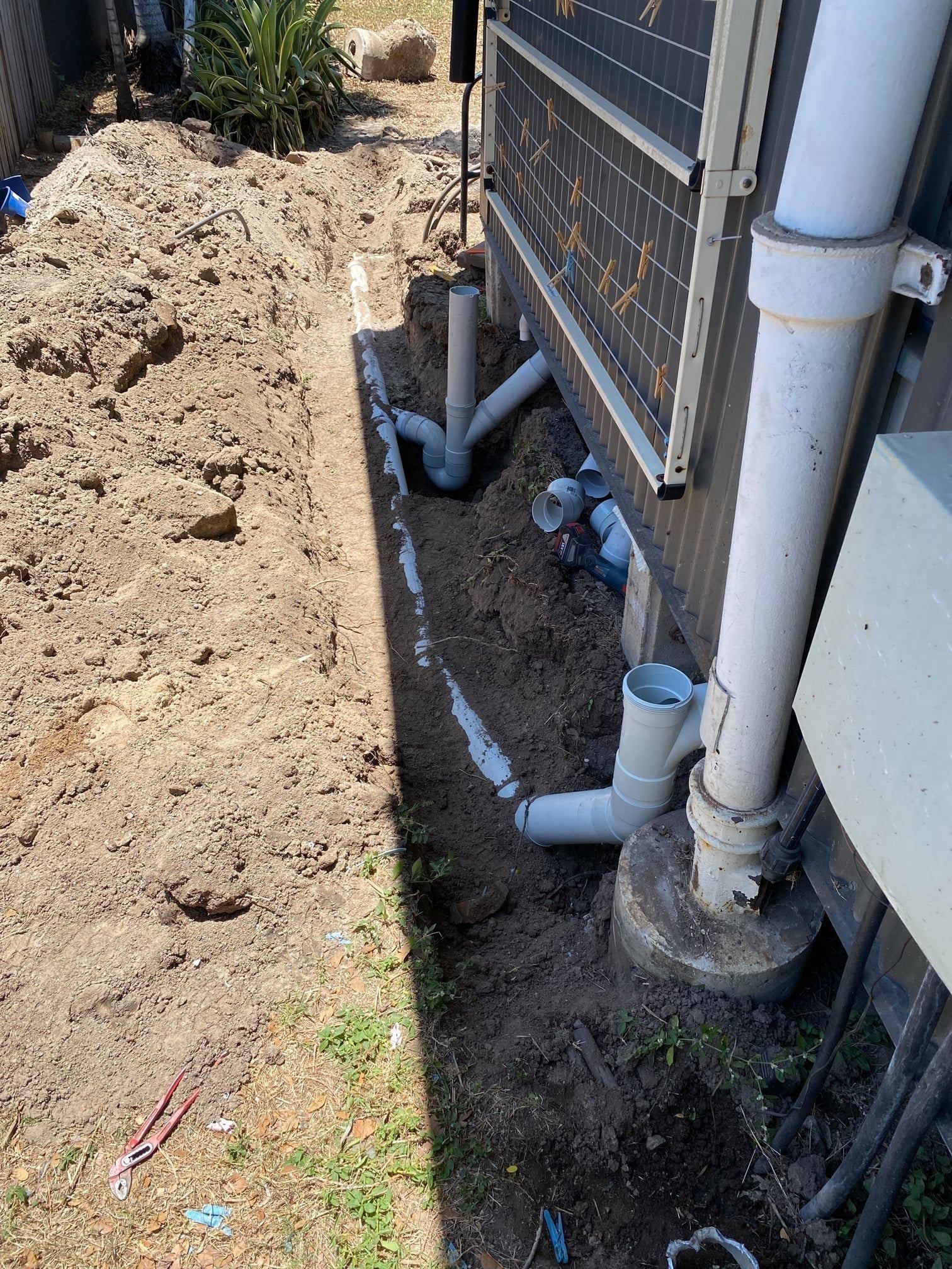 Trench With Exposed Plumbing Pipes Near a Building Foundation — Top To Bottom Plumbing in Garbutt, QLD