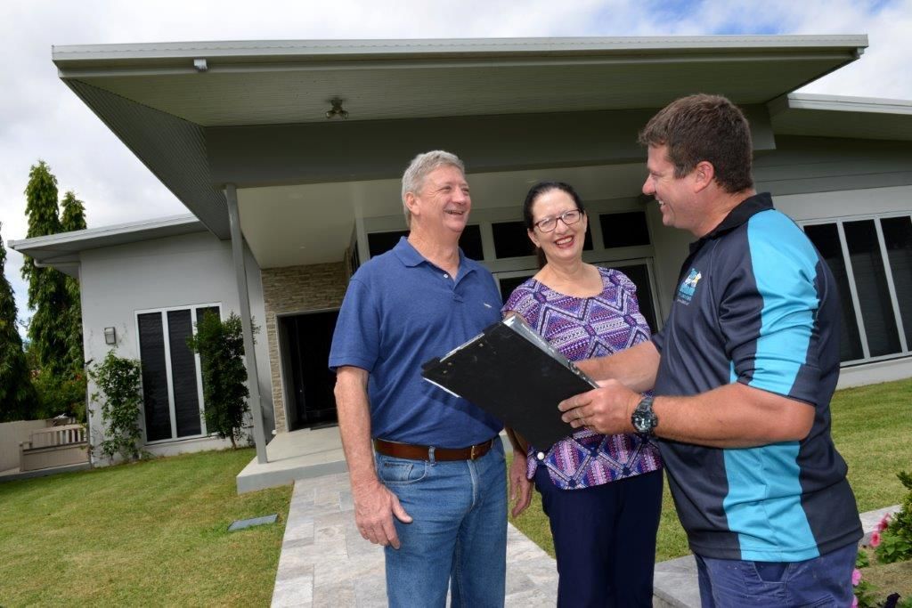 A real estate agent shows a couple a clipboard in front of a modern house — Top To Bottom Plumbing in Garbutt, QLD