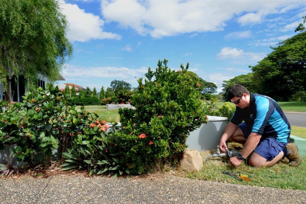 A Man Is Kneeling Down in A Kitchen Looking Under a Sink — Top To Bottom Plumbing in Garbutt, QLD