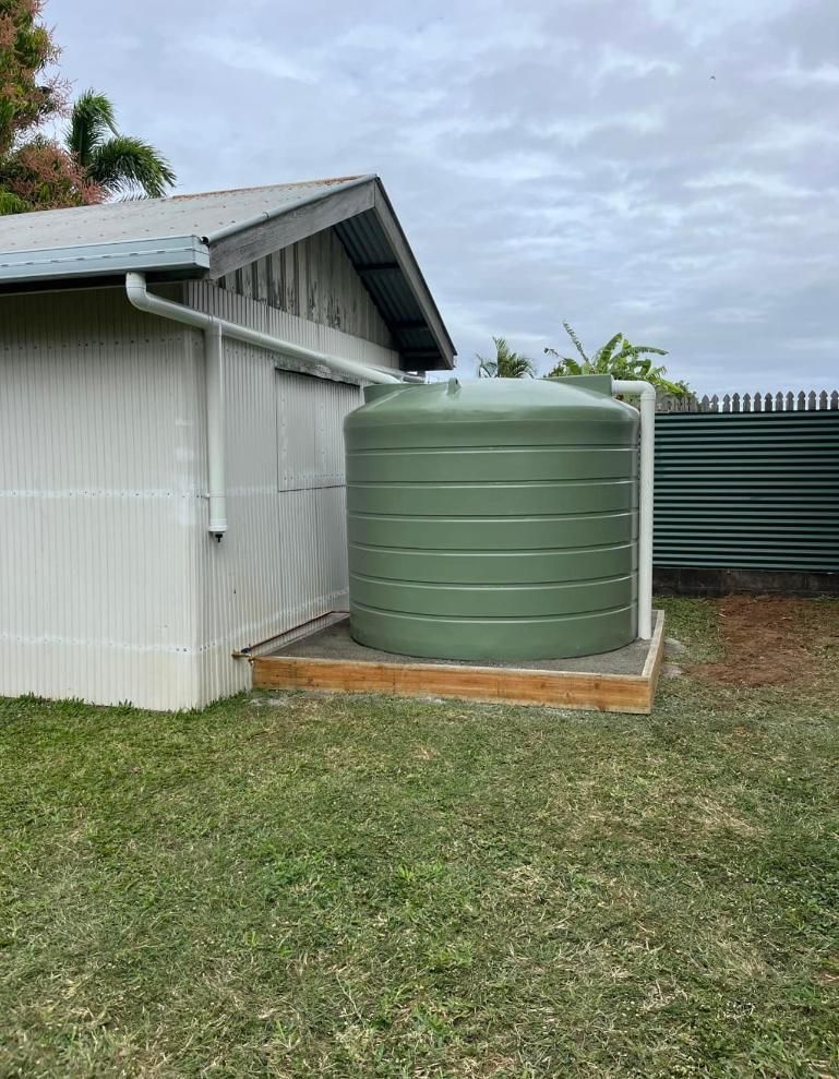 A Green Water Tank Is Sitting in The Grass Next to A House — Top To Bottom Plumbing in Garbutt, QLD