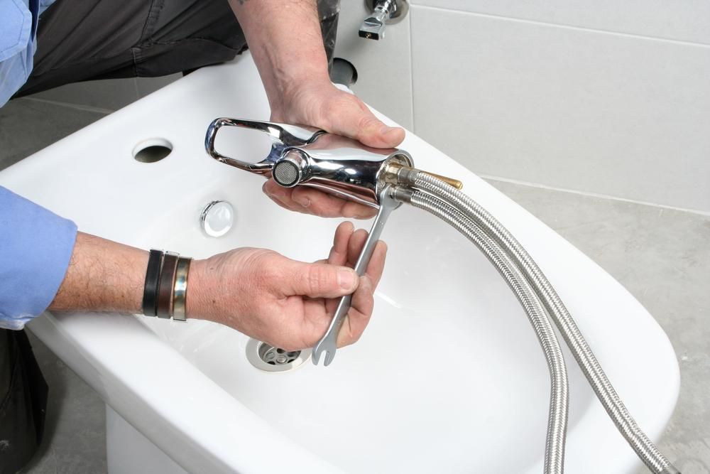 A Man Is Fixing a Bathroom Sink with A Wrench — Top To Bottom Plumbing in Garbutt, QLD