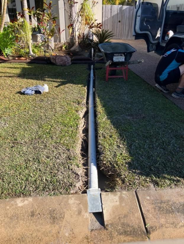 A Man Is Working on A Pipe in A Yard Next to A Wheelbarrow — Top To Bottom Plumbing in Garbutt, QLD