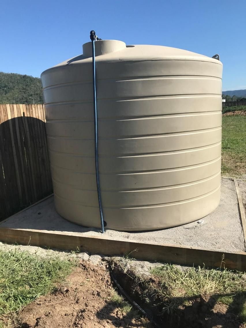 A Large Tan Water Tank Is Sitting in The Middle of A Grassy Field — Top To Bottom Plumbing in Garbutt, QLD