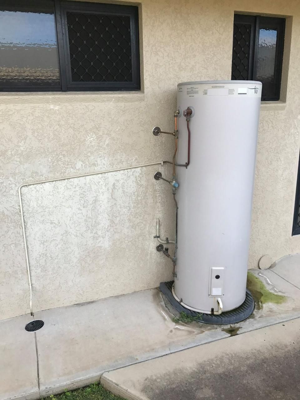 A White Water Heater Is Sitting on The Side of A Building — Top To Bottom Plumbing in Garbutt, QLD