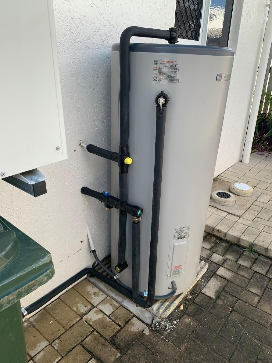 A Water Heater Is Sitting on A Brick Sidewalk Next to A Trash Can — Top To Bottom Plumbing in Garbutt, QLD