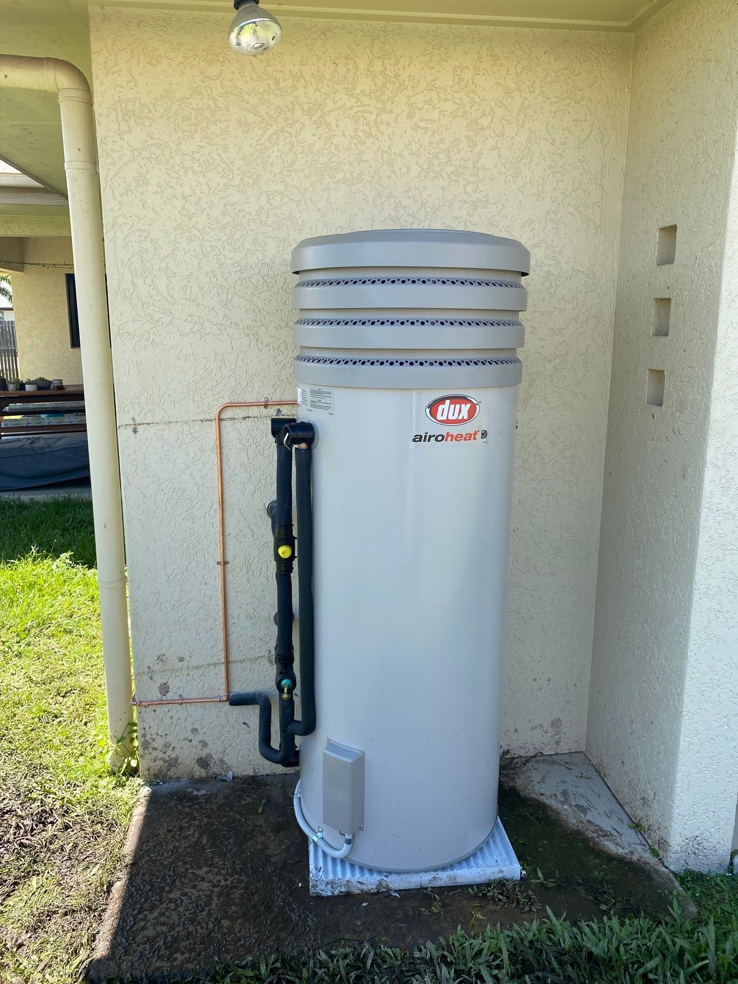 A Tall, Cylindrical Hot Water Heater Against a Stucco Wall — Top To Bottom Plumbing in Garbutt, QLD