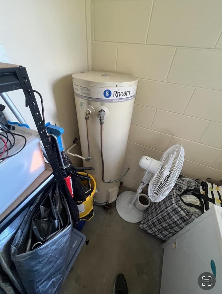 A Rheem Water Heater is Tucked in a Corner of a Utility Room With Beige Walls