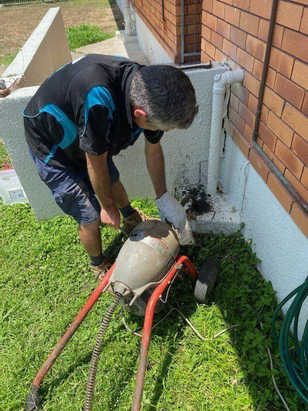A Man Is Using a Machine to Drain a Drain Outside of A House — Top To Bottom Plumbing in Garbutt, QLD