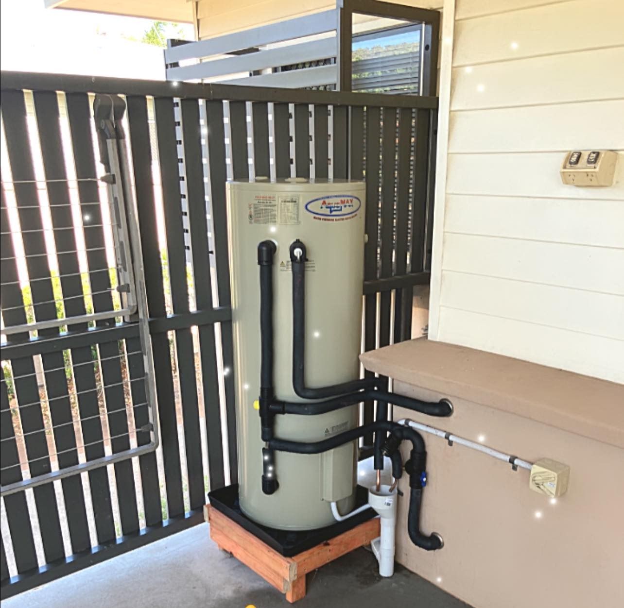 A Water Heater Is Sitting on The Side of A House Next to A Window — Top To Bottom Plumbing in Garbutt, QLD