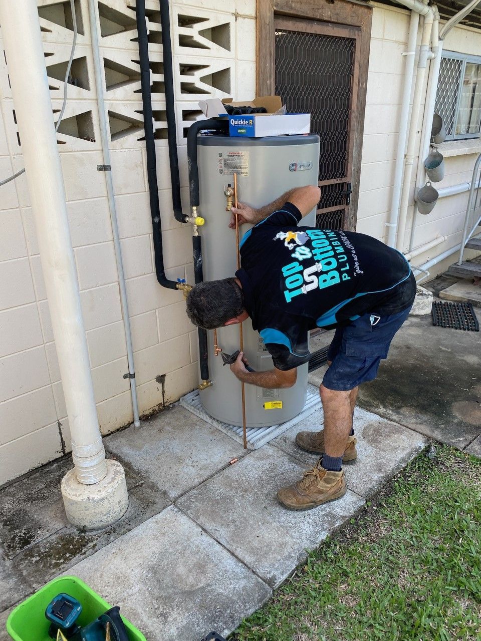 A Man Is Fixing a Toilet with Pliers — Top To Bottom Plumbing in Garbutt, QLD