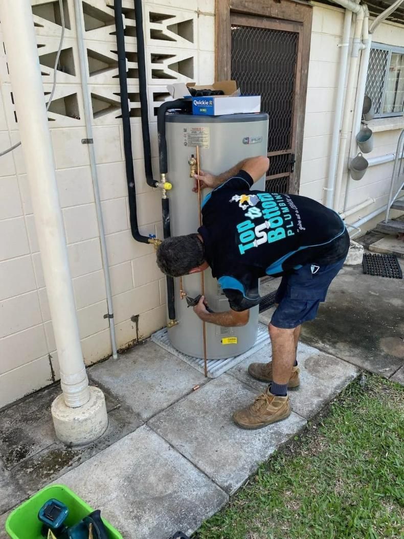 A Man Is Working on A Water Heater Outside of A House — Top To Bottom Plumbing in Garbutt, QLD