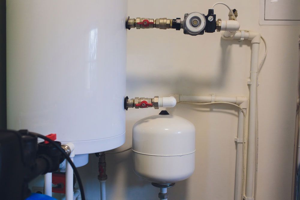 A White Water Heater Is Sitting Next to A White Tank in A Room — Top To Bottom Plumbing in Garbutt, QLD