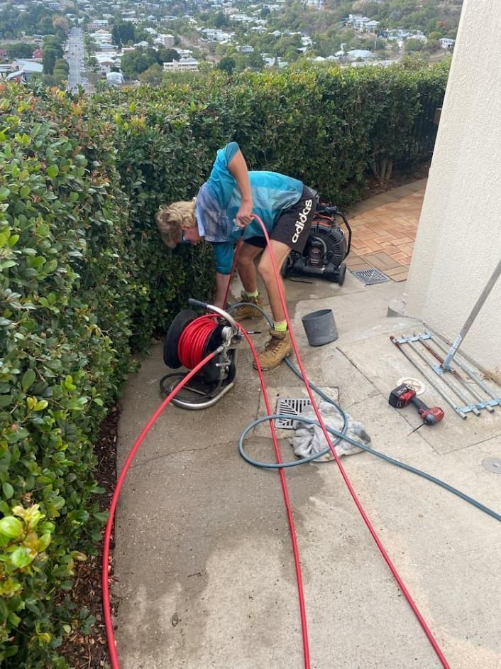 A Man Is Working on A Drain on The Side of A Building — Top To Bottom Plumbing in Garbutt, QLD