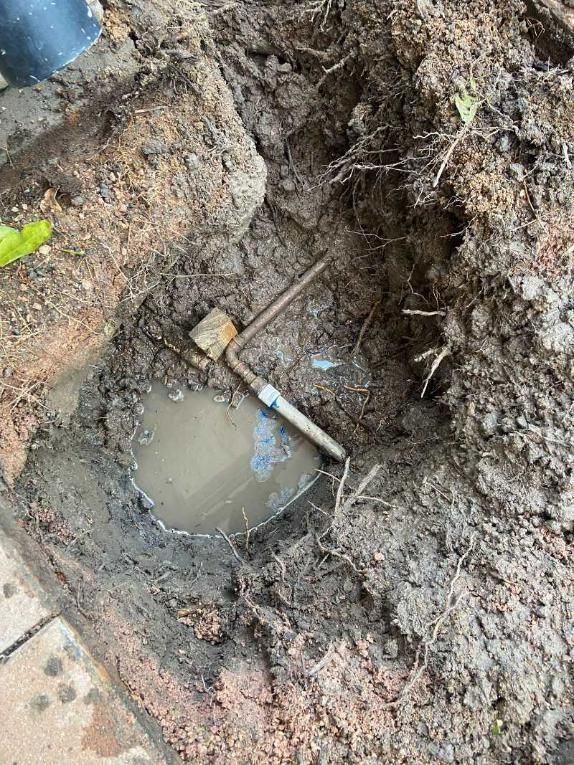 A Metal Pipe Is Laying in The Dirt Next to A Puddle of Water — Top To Bottom Plumbing in Garbutt, QLD