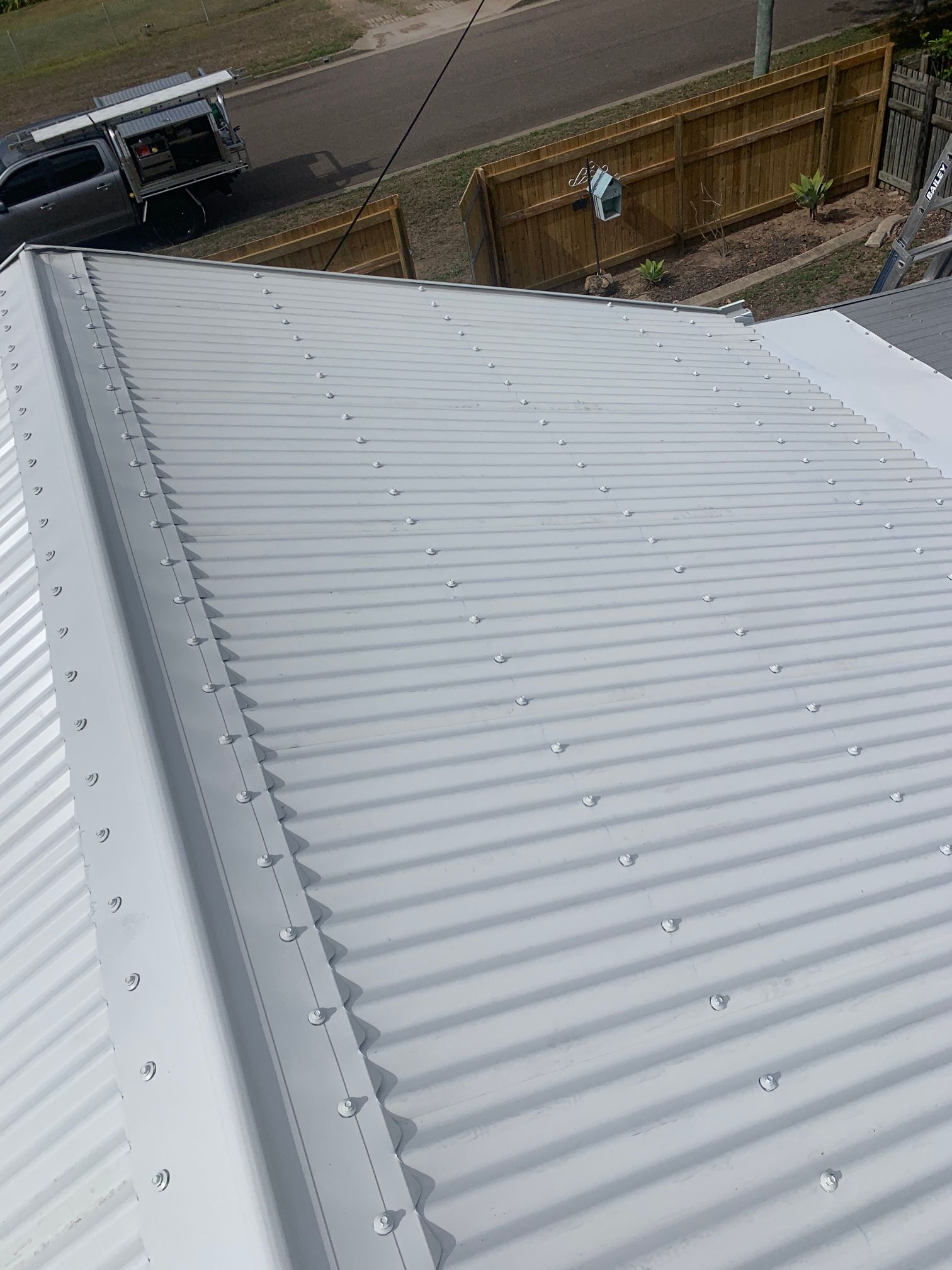 A Man Is Working on A Metal Roof with A Drill — Top To Bottom Plumbing in Garbutt, QLD