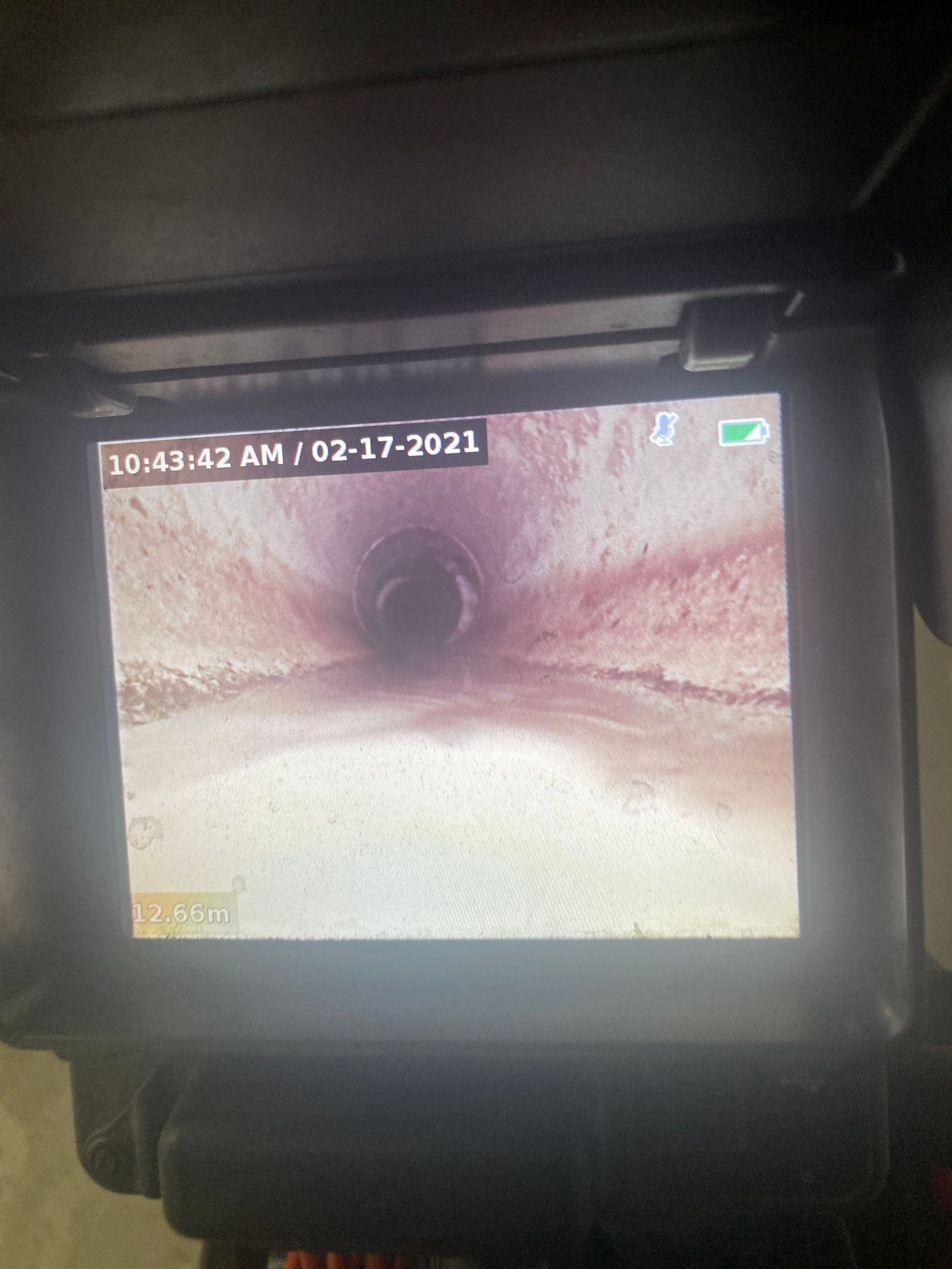 Drainage pipe view on a screen. Dark pipe center, surrounded by red/brown stains, water below. Timestamp shows date and time — Top To Bottom Plumbing in Garbutt, QLD