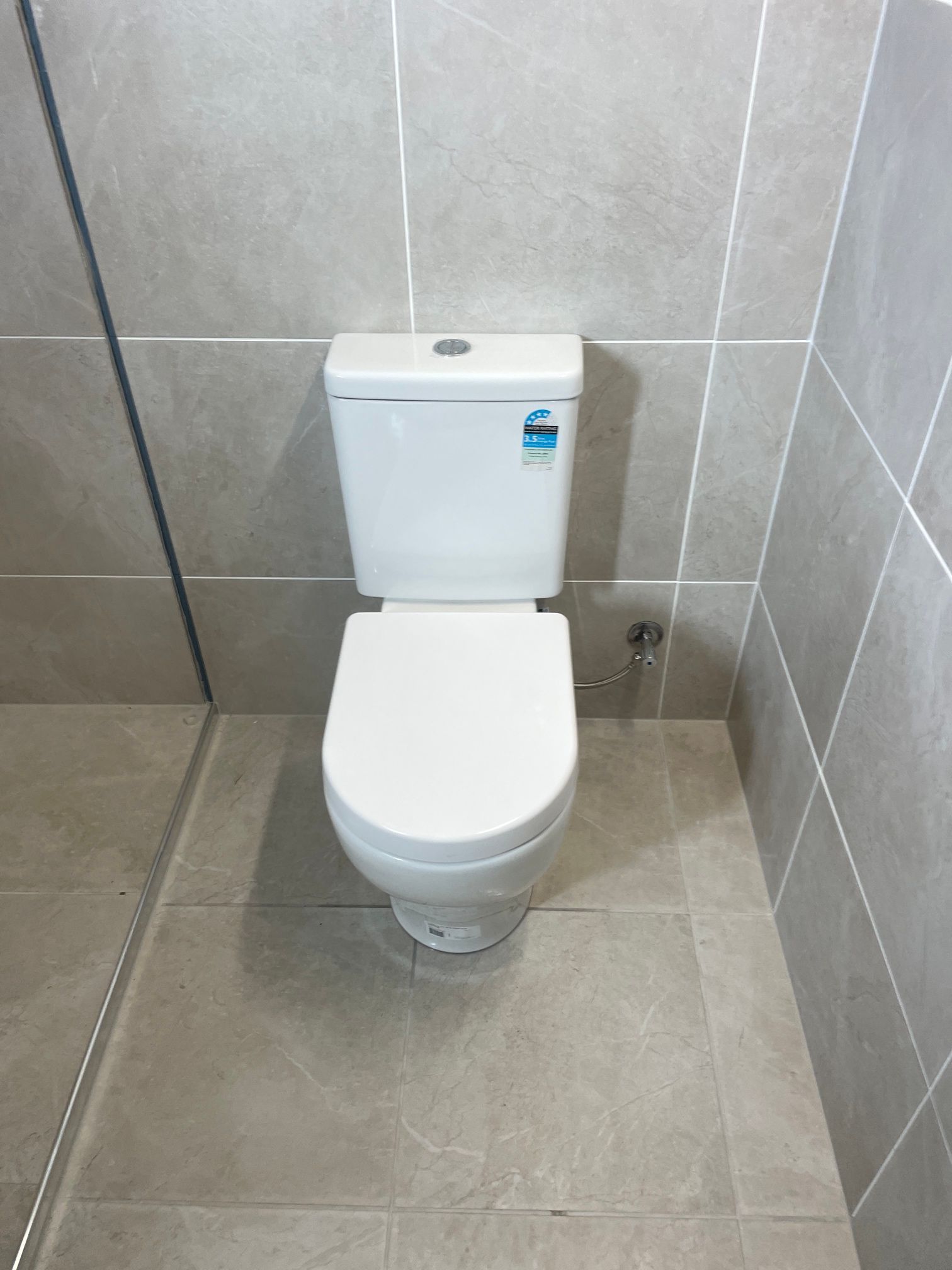 White toilet in a tiled bathroom. Grey floor and wall tiles. Water-efficient design — Top To Bottom Plumbing in Garbutt, QLD