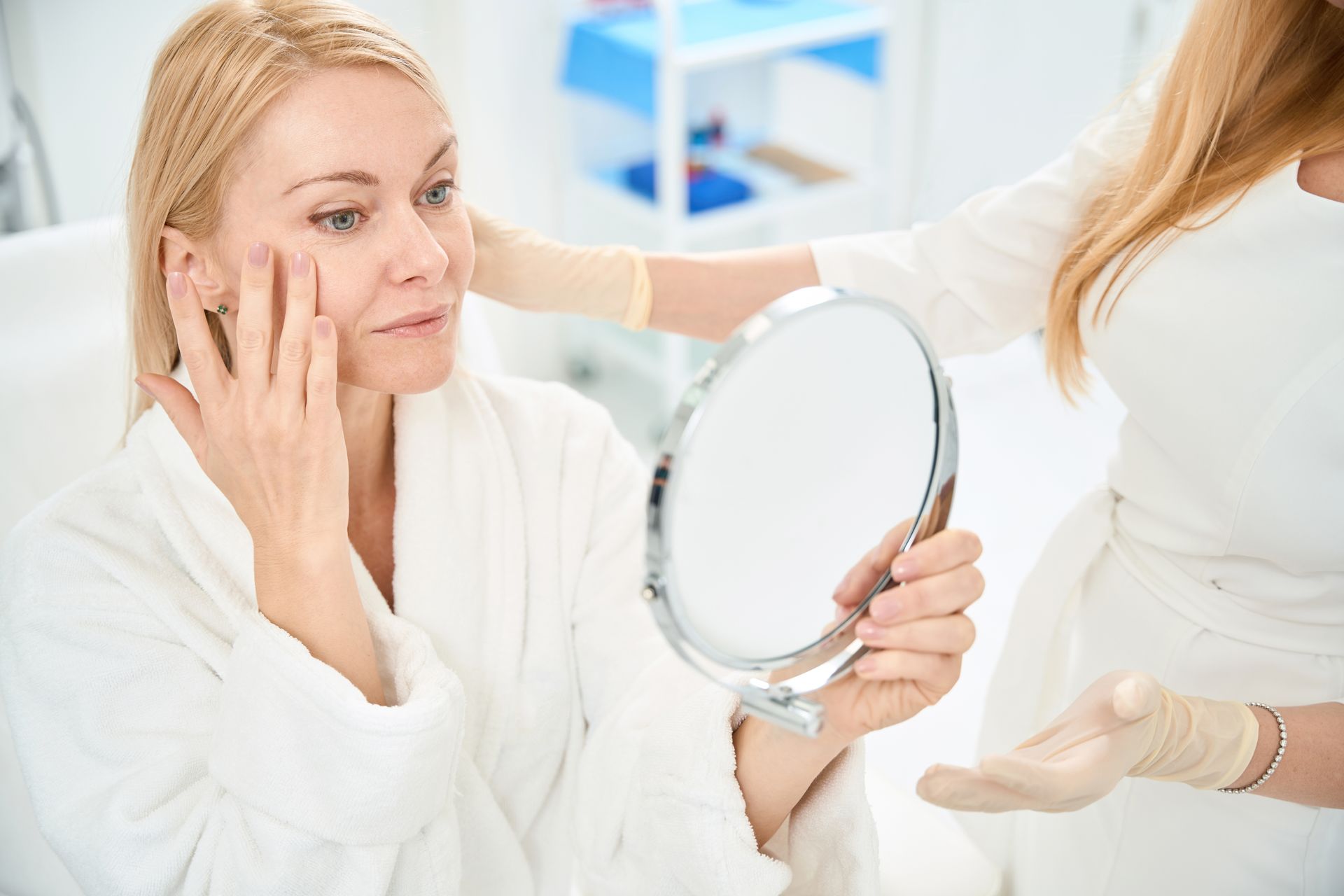 A woman is looking at her face in a mirror.