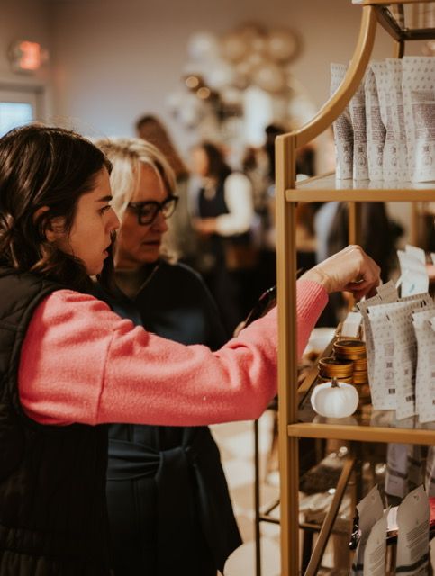 Two people in a shop browse products on a wooden shelf, with a focus on one reaching for a package.