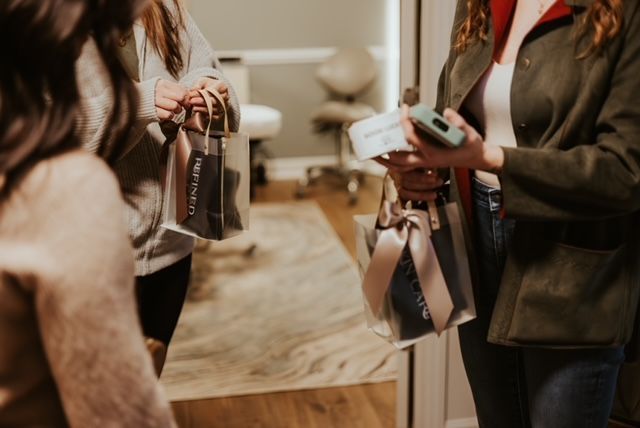 Three people in an interior space holding clear gift bags with ribbons, one person holding additional small boxed items.