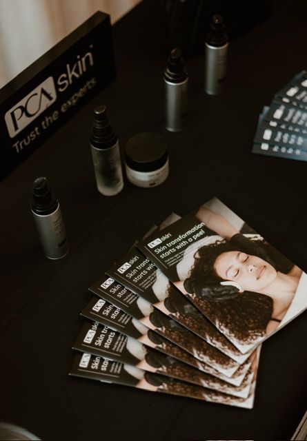 A PCA Skin display with bottles, a small jar, and a stack of pamphlets featuring a woman's face on a black surface.