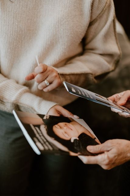 Two people hold and examine printed brochures featuring a photograph of a person, likely during a consultation.