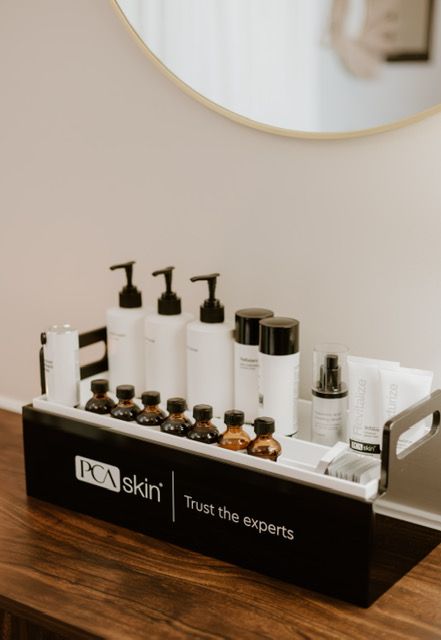 A branded PCA Skin black and white organizer filled with various skincare bottles and small vials on a wooden surface.