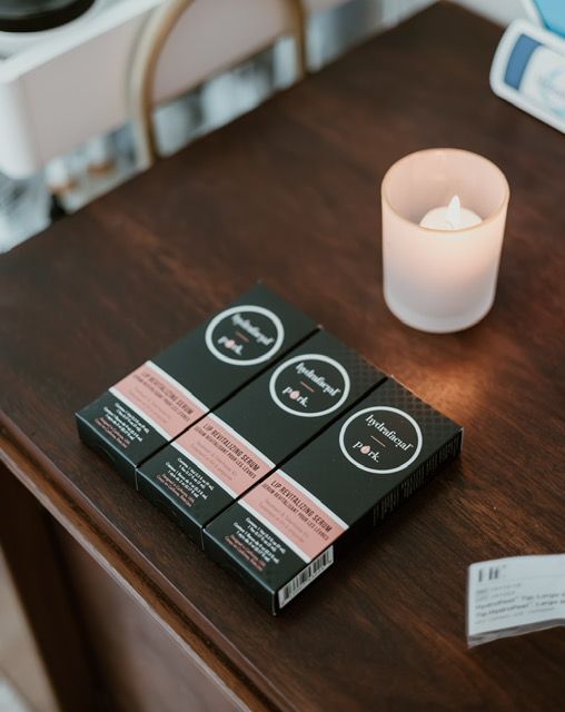 Three boxes of Apothecals lip products arranged on a dark wooden table next to a lit candle.