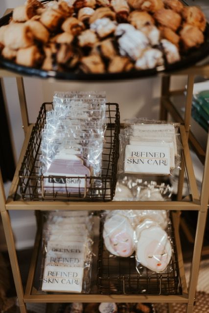 A tiered display cart holds a tray of pastries above two wire baskets containing cookies branded 
