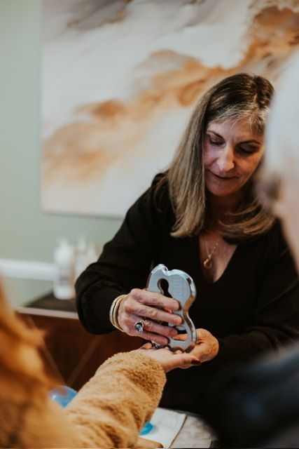 A professional uses a stainless steel Gua Sha tool to perform a massage on a person's hand in a spa or clinical setting.