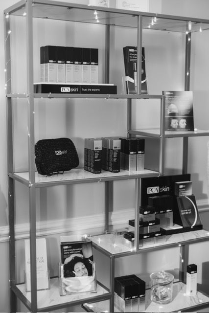 A metal shelving unit displaying assorted skincare products, boxes, and pamphlets in a retail or clinic setting.