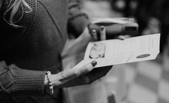 A person holds a flyer in one hand and a mobile payment device in the other, standing in a brightly lit indoor space.