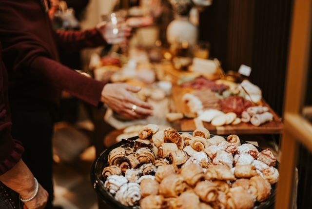 People reaching for an assortment of pastries and charcuterie at a table during a social gathering.