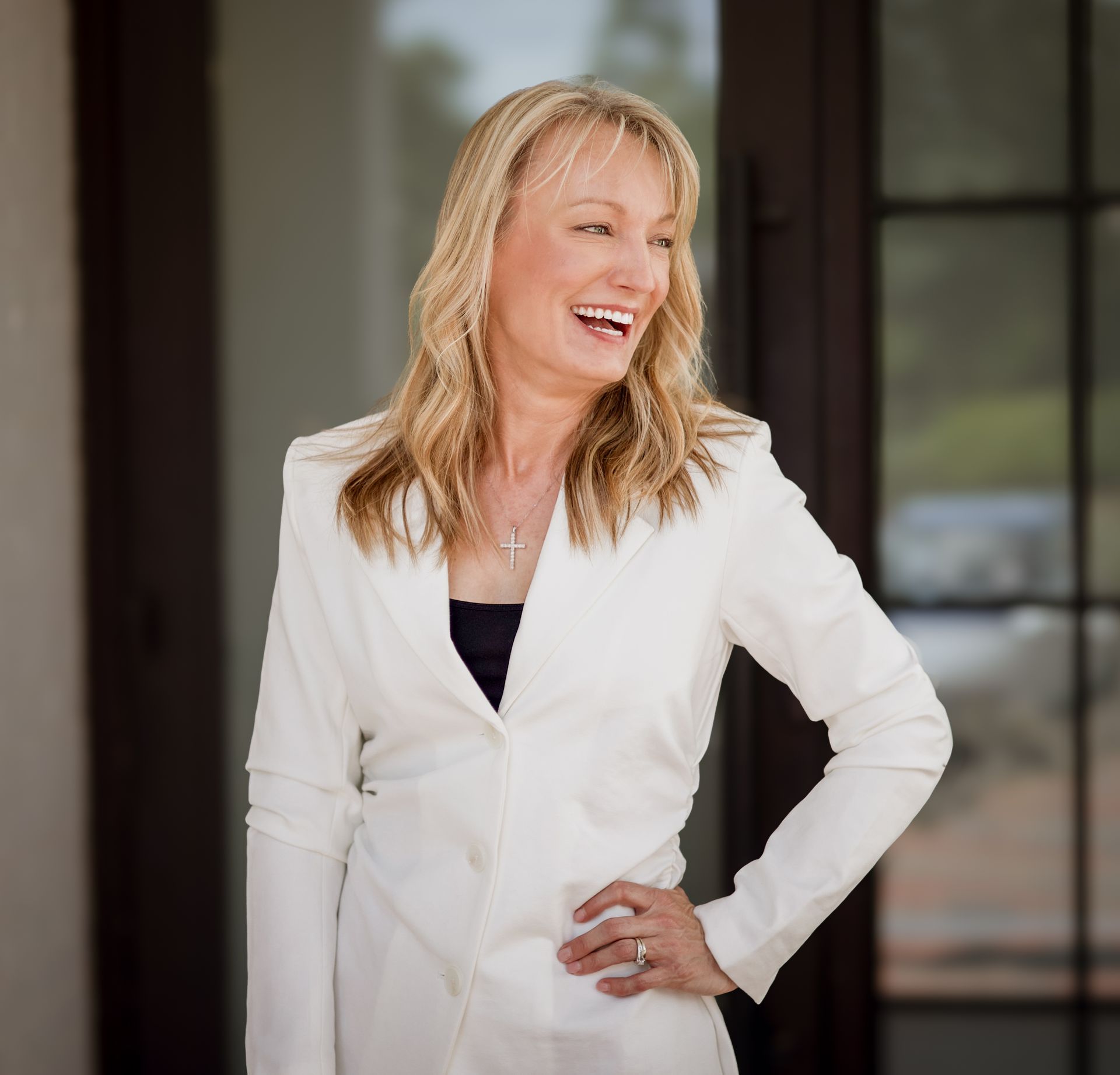 A woman in a white suit is laughing with her hands on her hips.