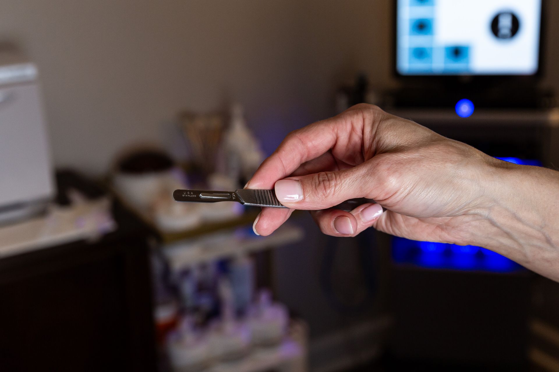 A woman is holding a dermaplane scalpal in her hand.