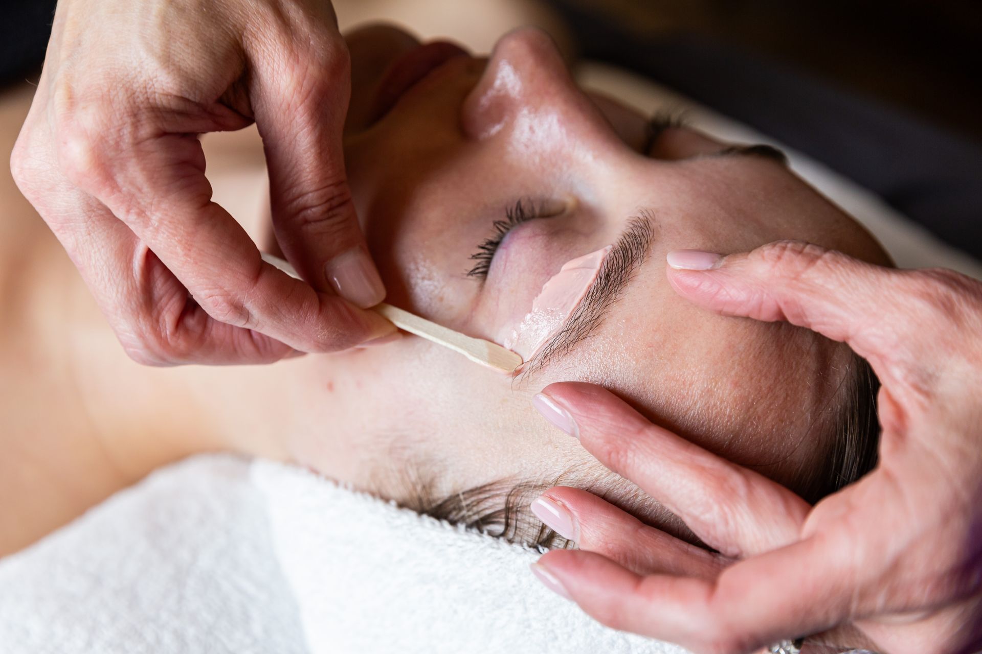 Person getting eyebrow waxed; aesthetician applies wax with a spatula.