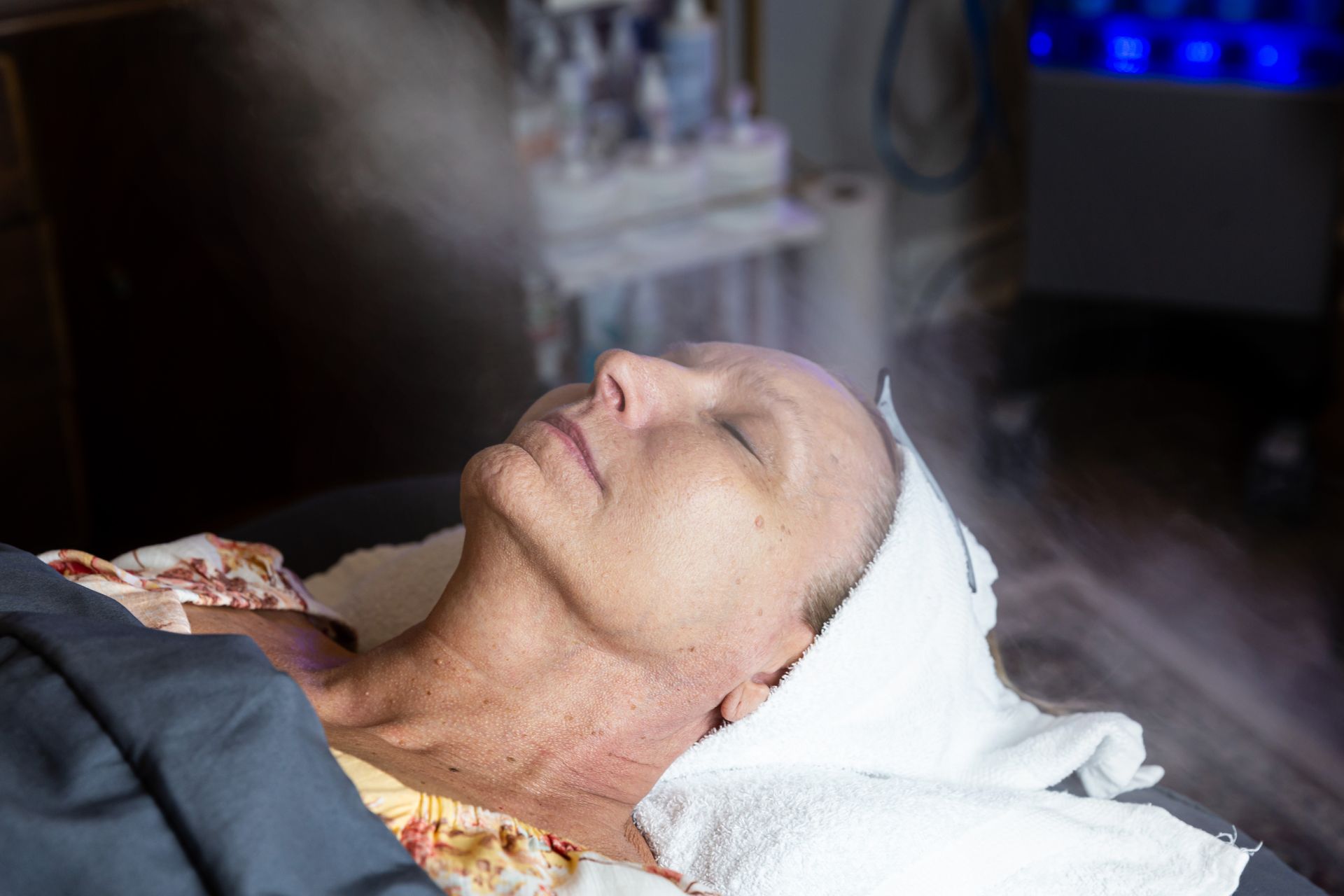 A woman is laying on a bed with her eyes closed and getting a facial treatment.