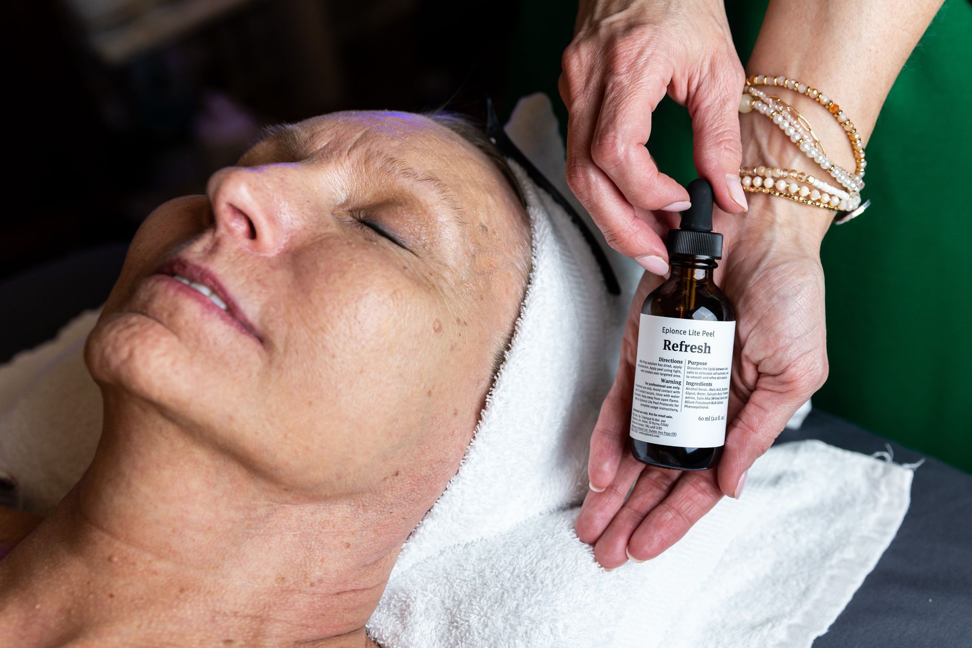A woman is getting a facial treatment with a bottle of lotion on her face.