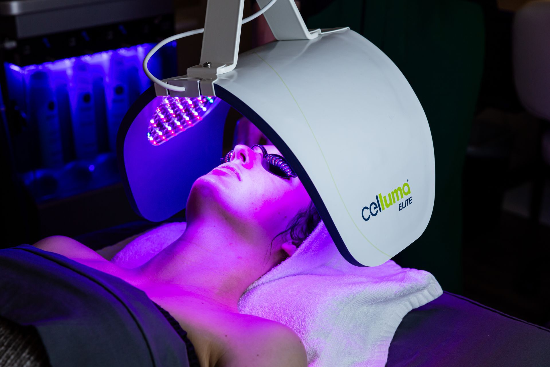 A woman is laying on a bed with a purple light on her head.