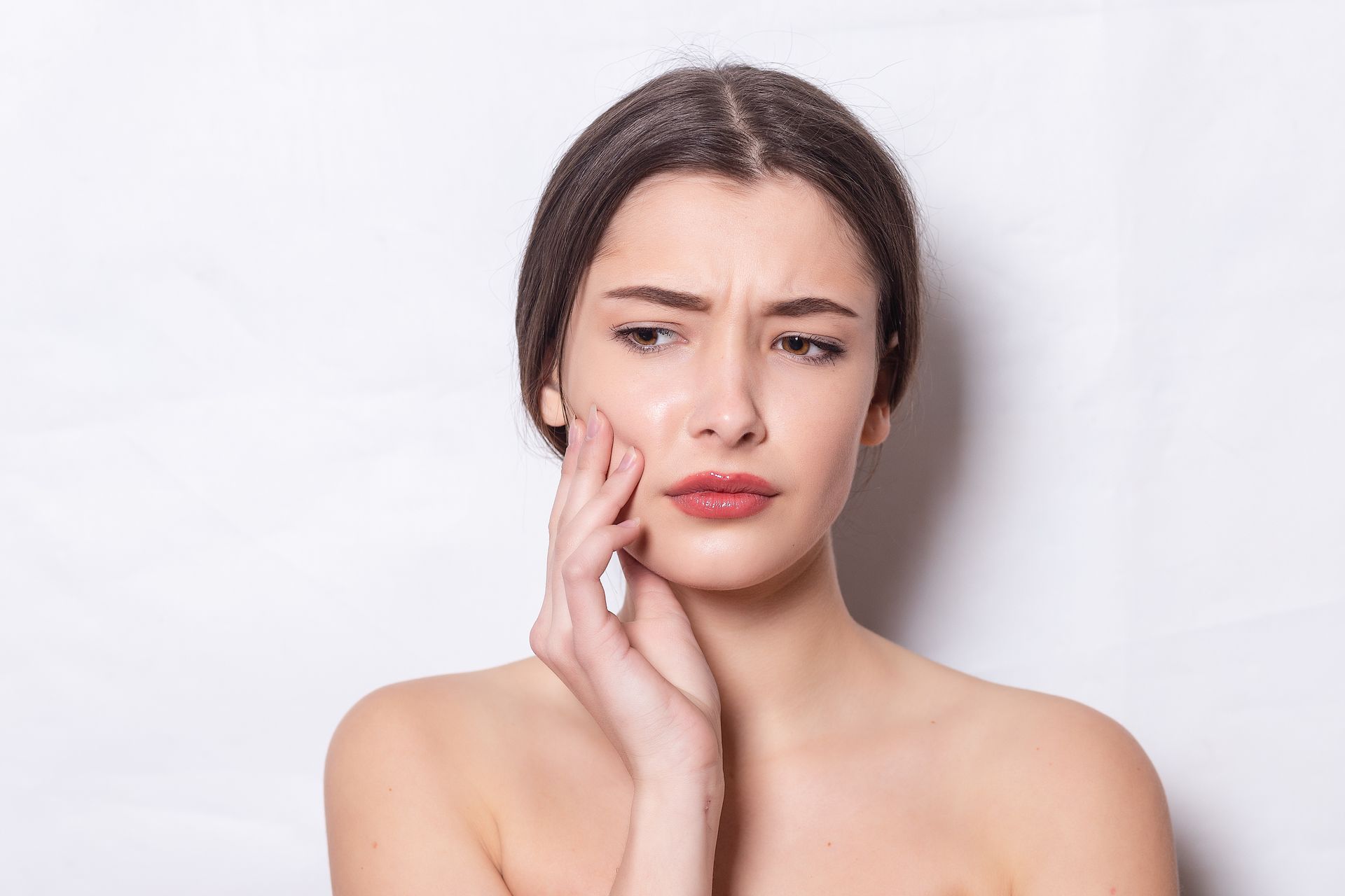 A person with a pained expression holding their hand to their cheek, suggesting a toothache against a white background.