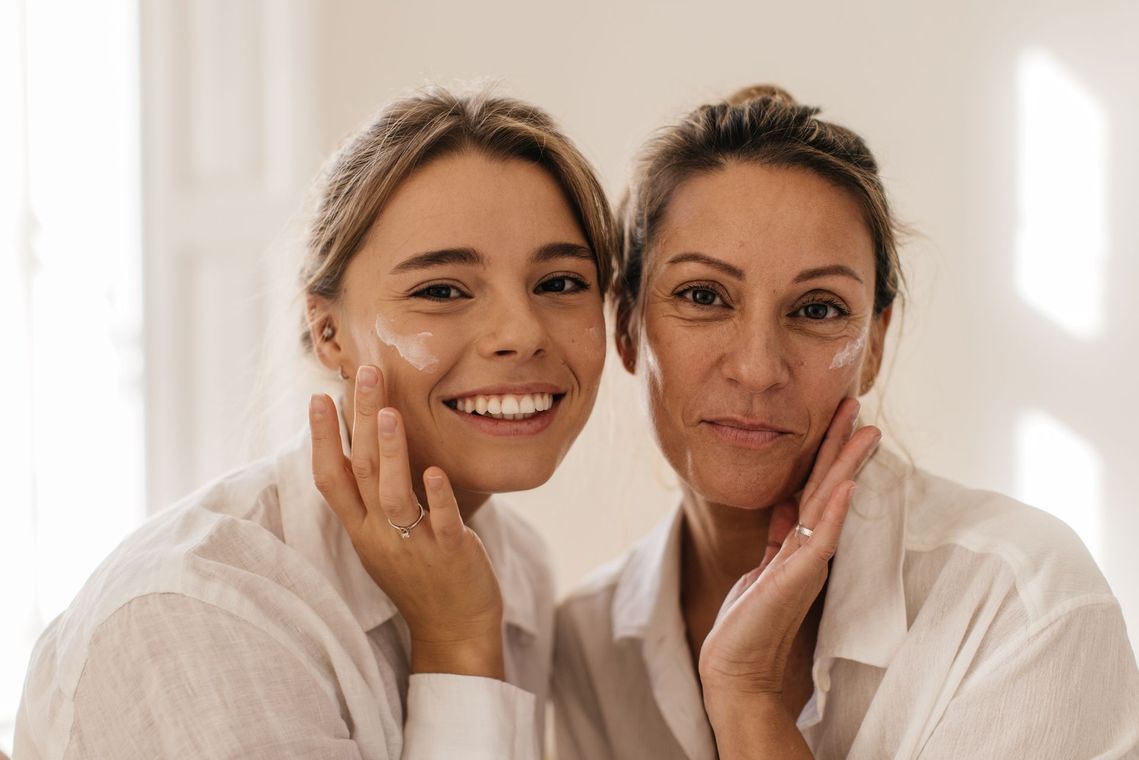 A young woman and an older woman are applying cream to their faces.