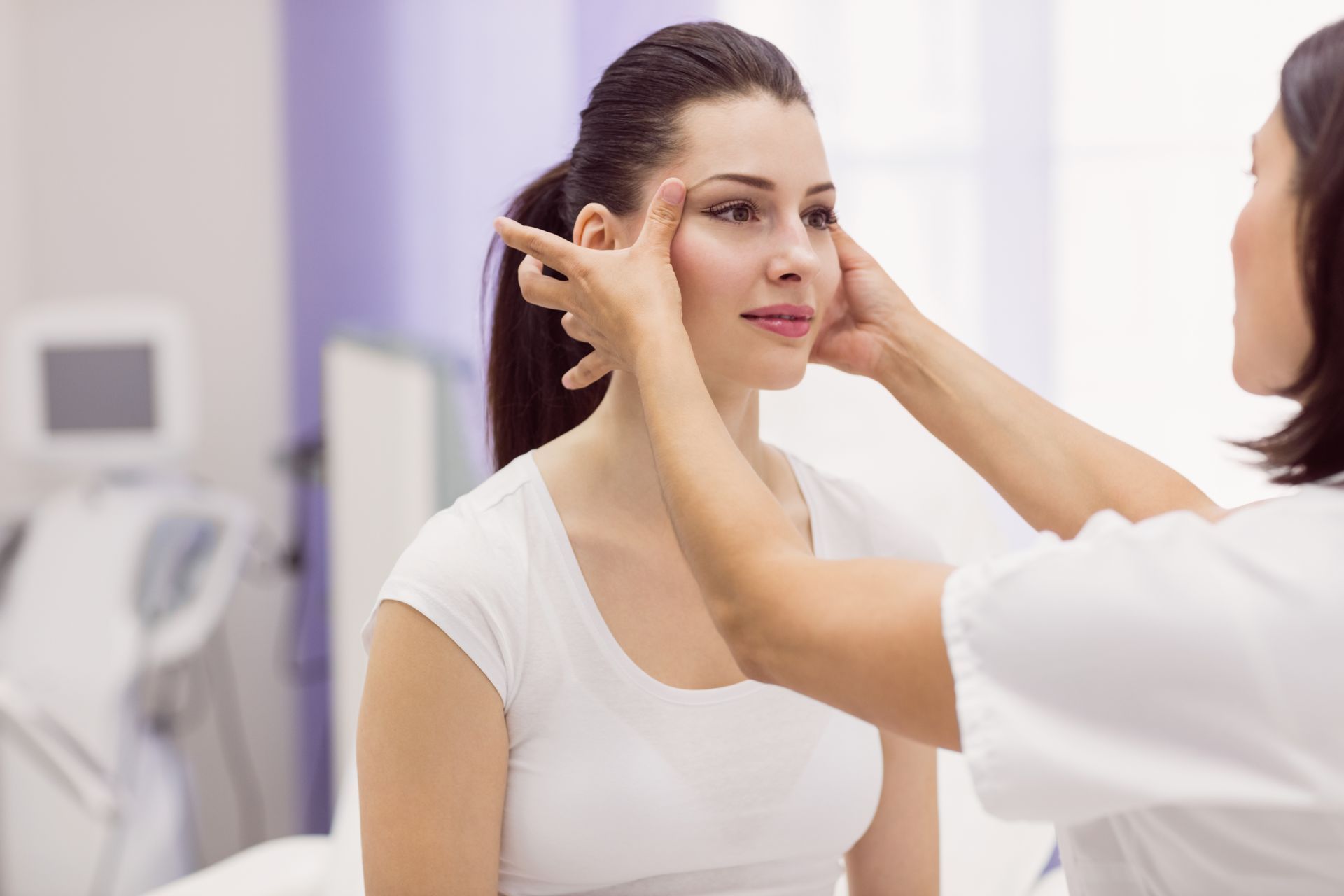 Woman having face examined by a medical professional in a clinic setting.