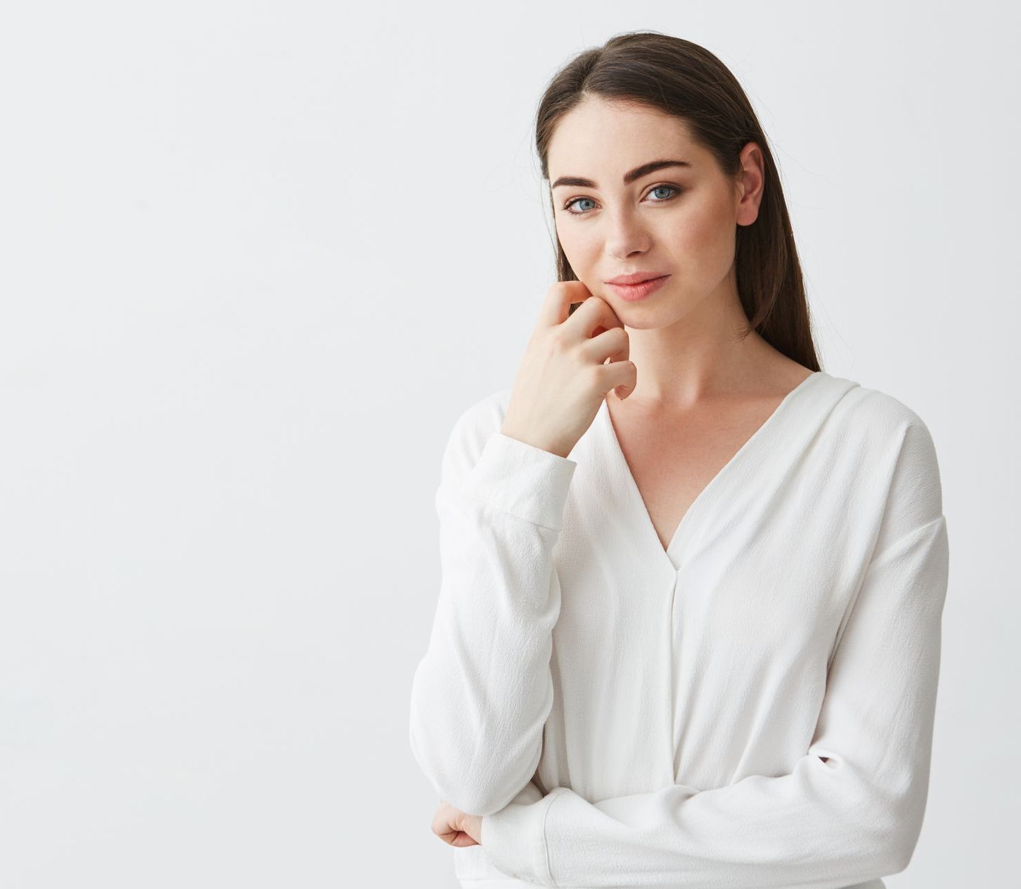 A woman in a white shirt is holding her hand to her chin.