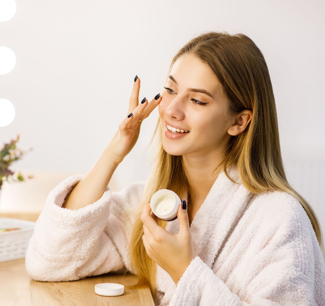 A woman is applying cream to her face in front of a mirror.